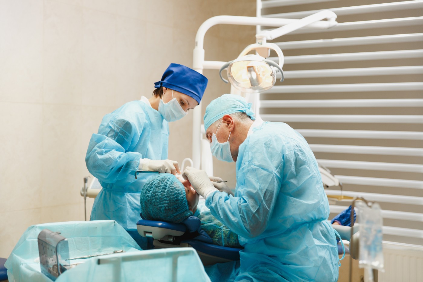 Male dentist surgeon in uniform and female assistant helps to performing operation